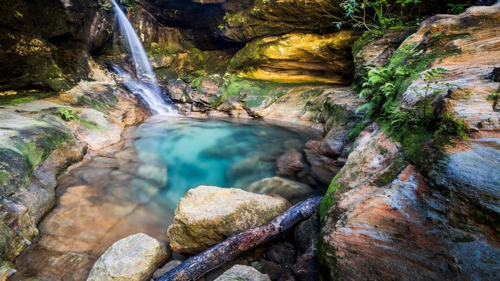 Waterfall cascading into a clear turquoise pool surrounded by mossy rocks
