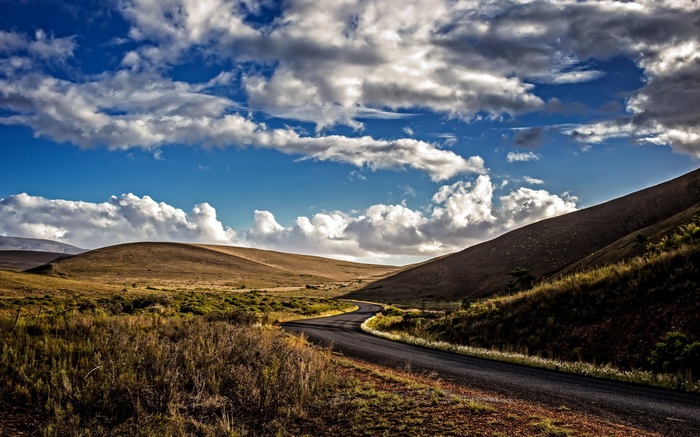 Winding road through rolling hills under a cloudy sky