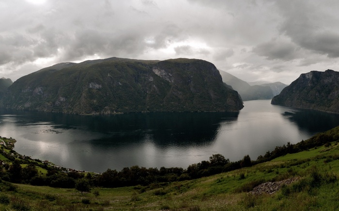 Panoramic view of a fjord with steep, tree-covered mountains under a cloudy sky