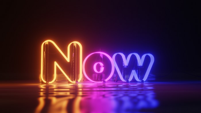 Neon sign spelling NOW with reflections