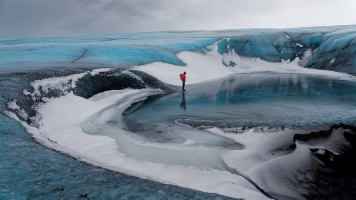 Person on a glacier with a blue ice lake