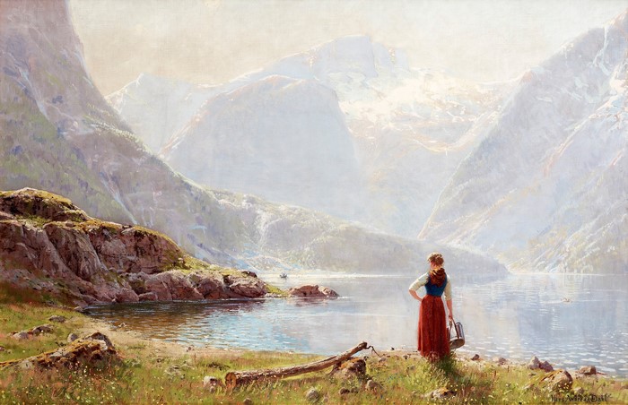 Woman in traditional dress by a fjord with mountains