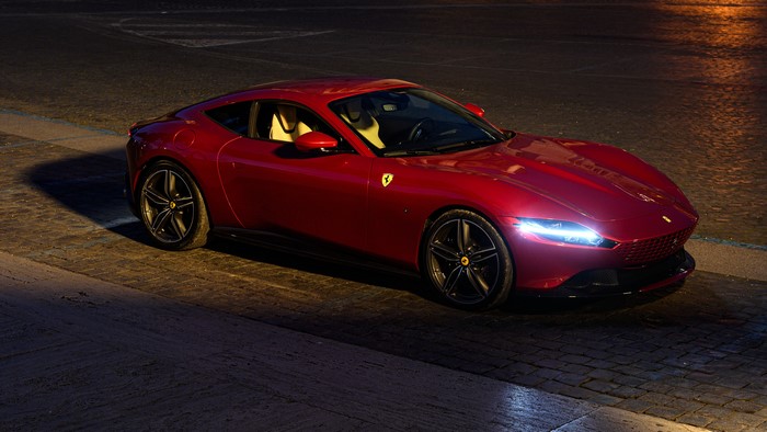 Red Ferrari Roma supercar parked on cobblestone street at night