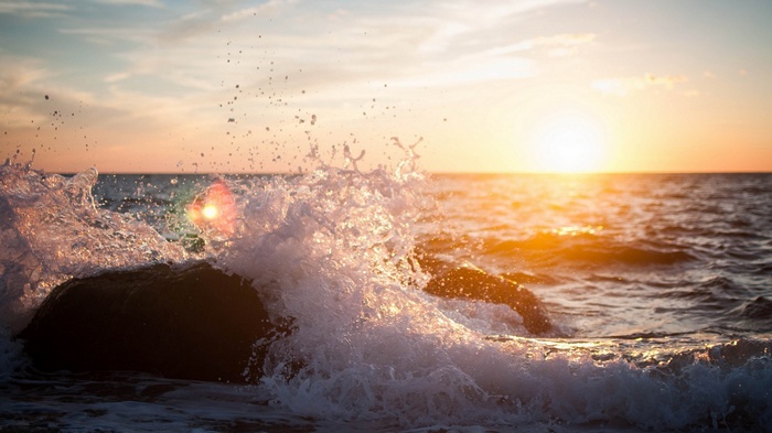 Wave crashing on rocks at sunset