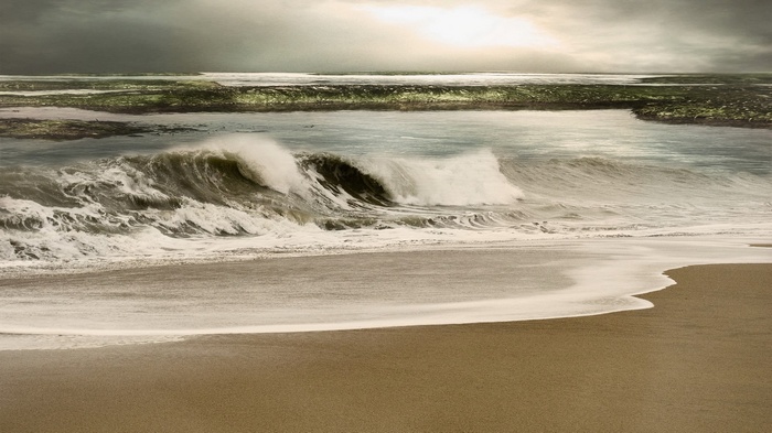 Waves crashing on a sandy beach under a cloudy sky