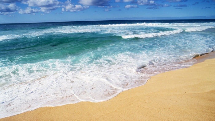 Ocean waves crashing on a sandy beach under a blue sky