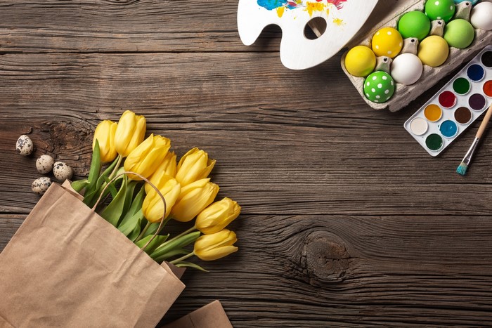 Easter eggs, tulips, and painting supplies on wooden table