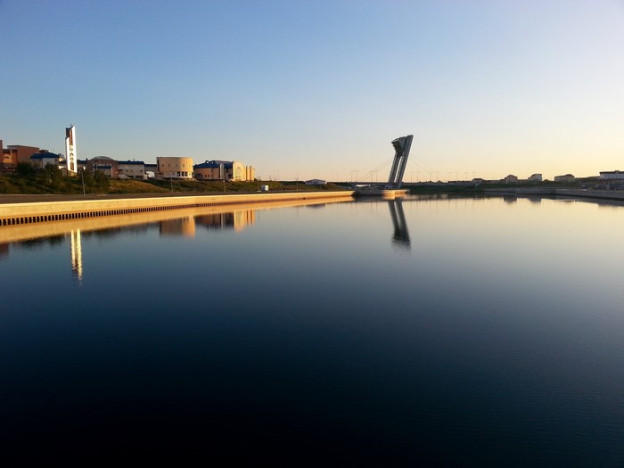 Modern architecture and bridge reflected in calm water at sunrise
