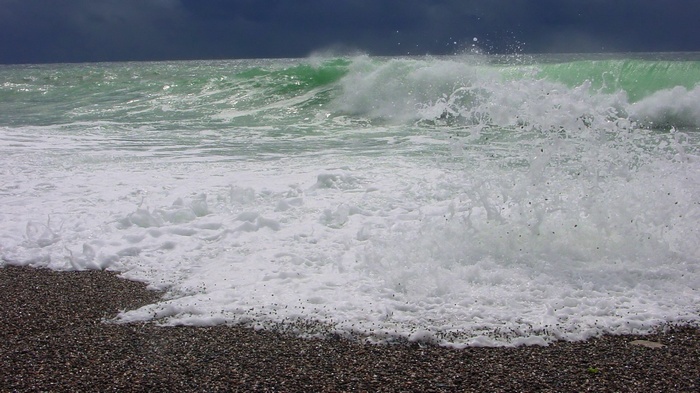 Waves crashing on a pebble beach under a dark sky