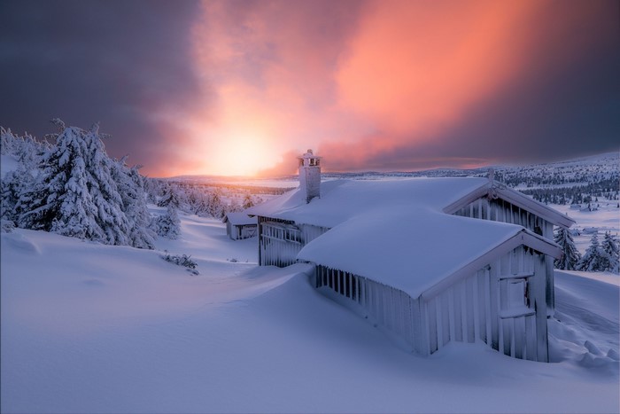 Snow-covered cabins during a vibrant sunset