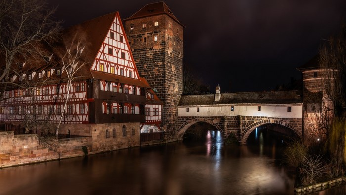 Half-timbered building and bridge over river at night in Nuremberg