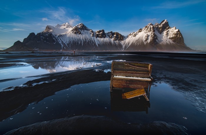 Old piano on a black sand beach with snowy mountains
