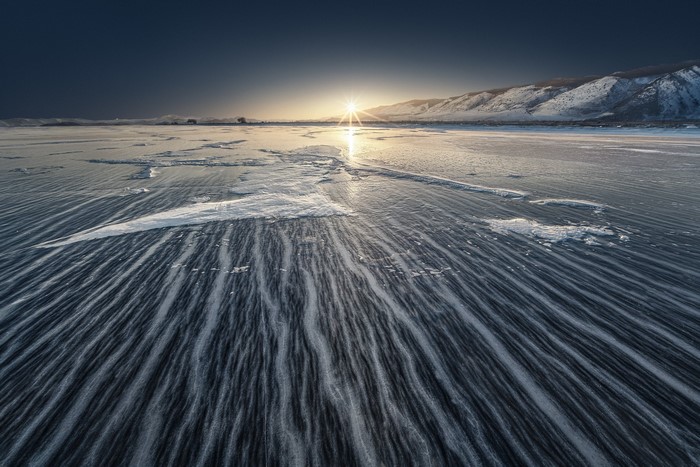 Winter landscape with sun over icy plains and mountains