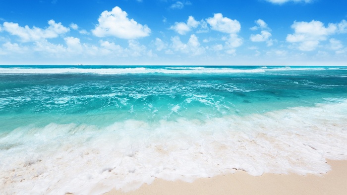Ocean waves crashing on a sandy beach under a blue sky