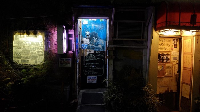 Nighttime entrance to a Japanese bar with posters and graffiti