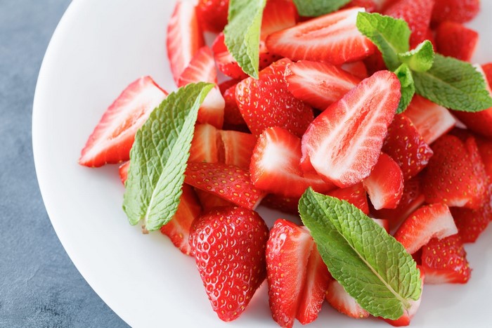 Sliced strawberries with mint leaves on a white plate