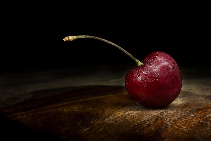 Single cherry with stem on wooden surface