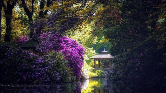 Gazebo by a pond surrounded by colorful flowers and trees
