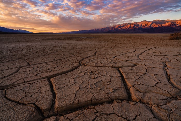 Cracked desert ground at sunset with mountains
