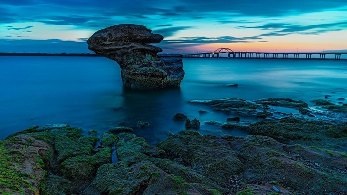 Rock formation in water with bridge at sunset