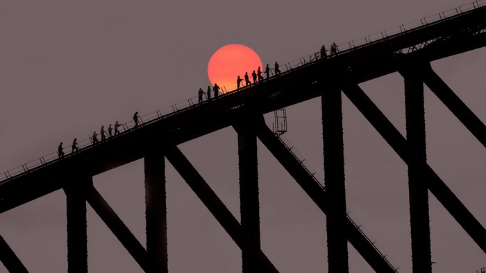 People climbing Sydney Harbour Bridge at sunset
