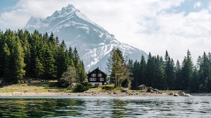 House by a lake with pine trees and snowy mountains