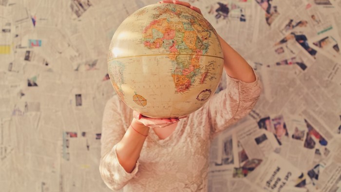 Woman holding a globe in front of a newspaper wall
