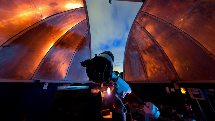 Telescope in observatory dome under starry sky