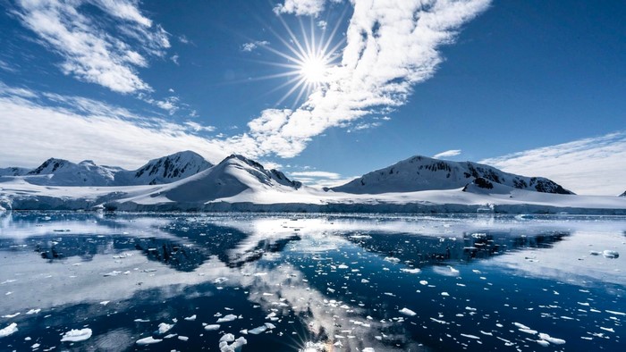 Snowy mountains reflected in icy water under a sunny sky