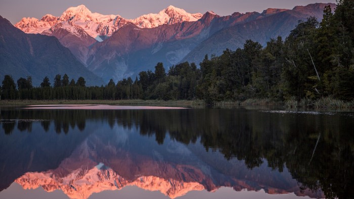 Snowy mountains reflecting in a lake at sunset