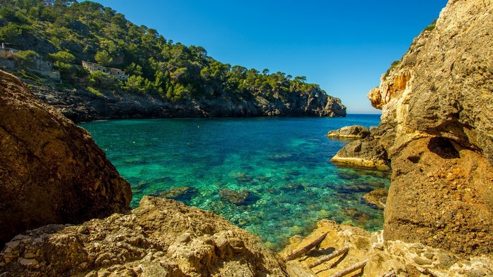 Clear turquoise water in a rocky cove with forested hills