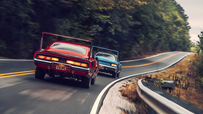 Two classic muscle cars racing on a winding road