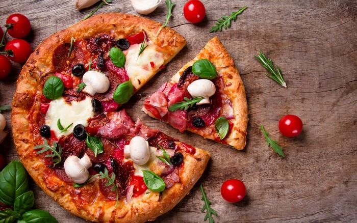 Pizza with pepperoni, mushrooms, olives, and basil on a wooden surface