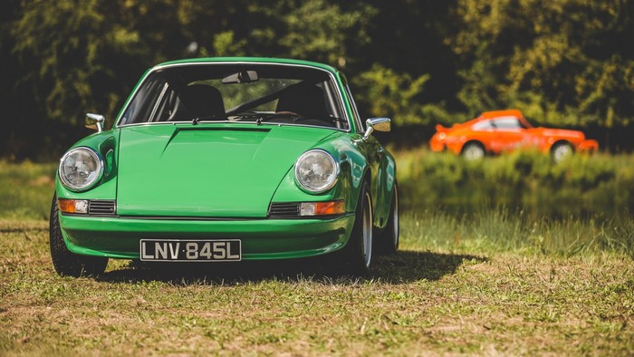 Green Porsche 911 and orange Porsche 911 on grass