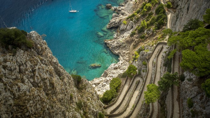 Winding path on a cliff overlooking the sea with a sailboat