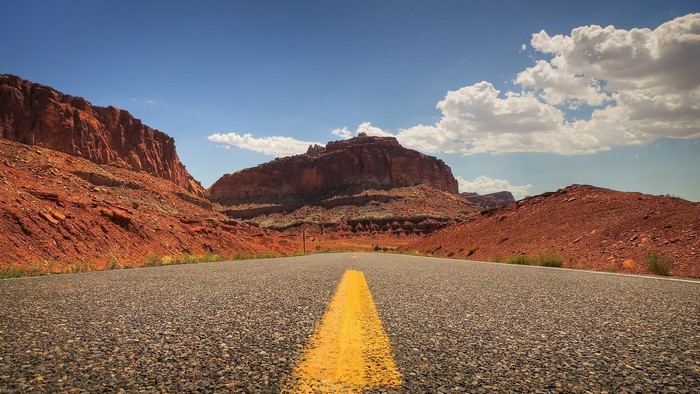 Road through red rock landscape under blue sky with clouds