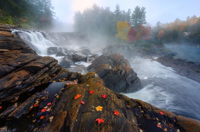 Waterfall in autumn with fallen leaves and fog