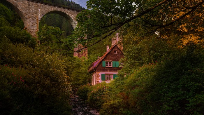 Stone bridge arching over a forest cabin