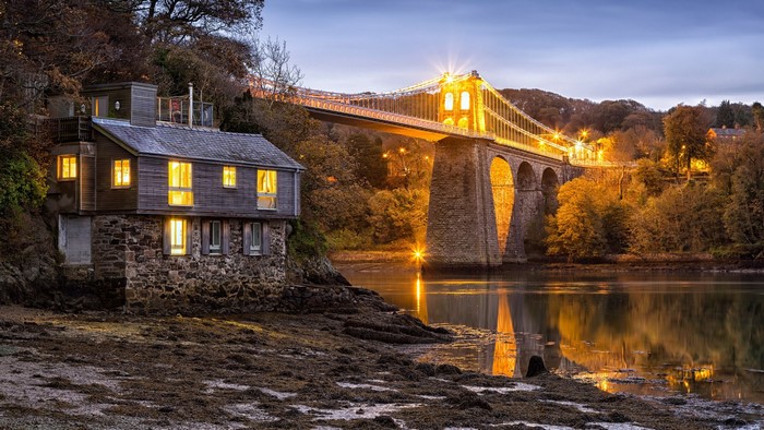 Stone house and illuminated bridge over river at dusk