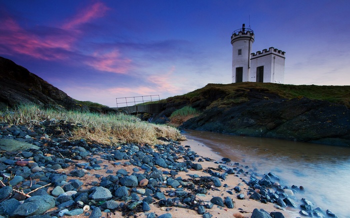 White lighthouse on a rocky shore at sunset