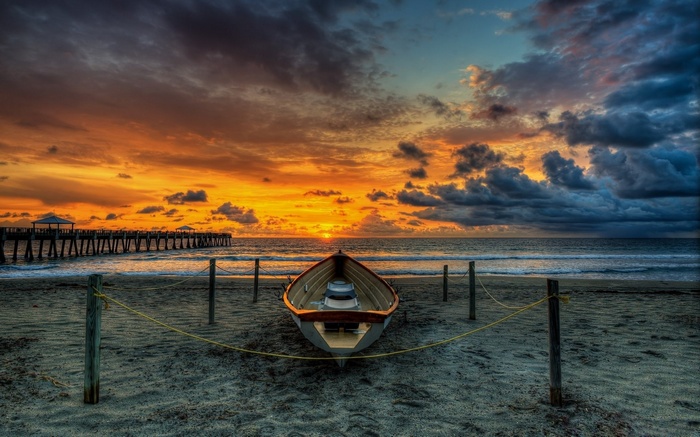Boat on beach with pier at sunset