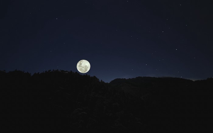 Full moon over dark hills at night