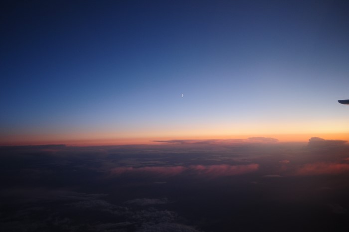 Airplane view of sunset over clouds with crescent moon