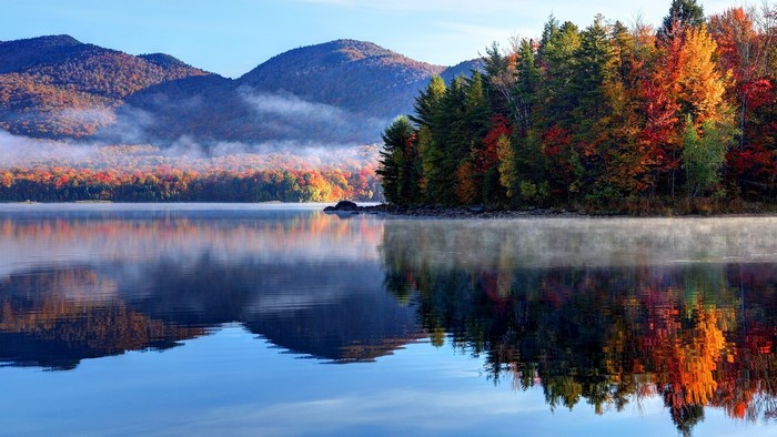 Autumn forest reflected in a misty lake with mountains