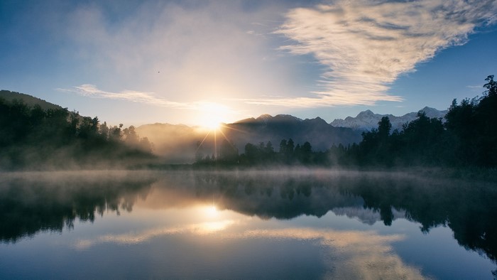 Lake Matheson sunrise with misty mountains and forest reflection