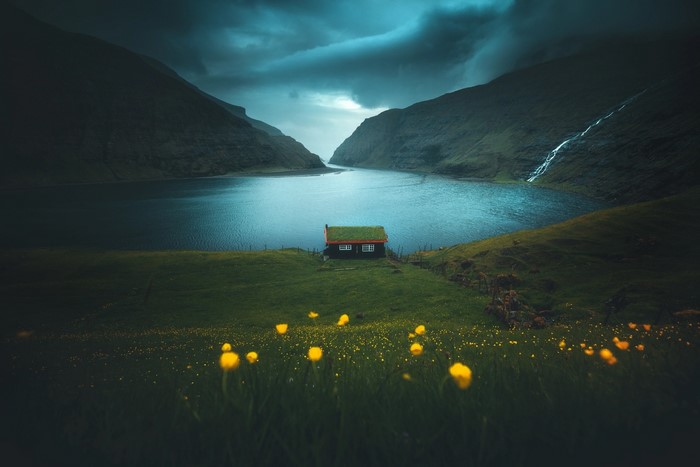 A small house with a green roof by a fjord