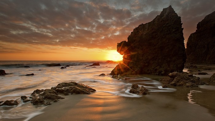 Sunset over the ocean with rock formations on the beach