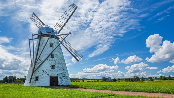 White windmill in a green field under a blue sky with clouds