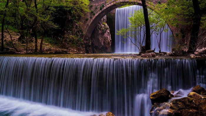 Waterfall flowing under a stone bridge in a forest