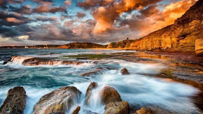 Sunrise over rocky coast with ocean waves and dramatic clouds